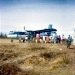 Late 1060s. Twin Otter mail plane on dirt strip behind town.